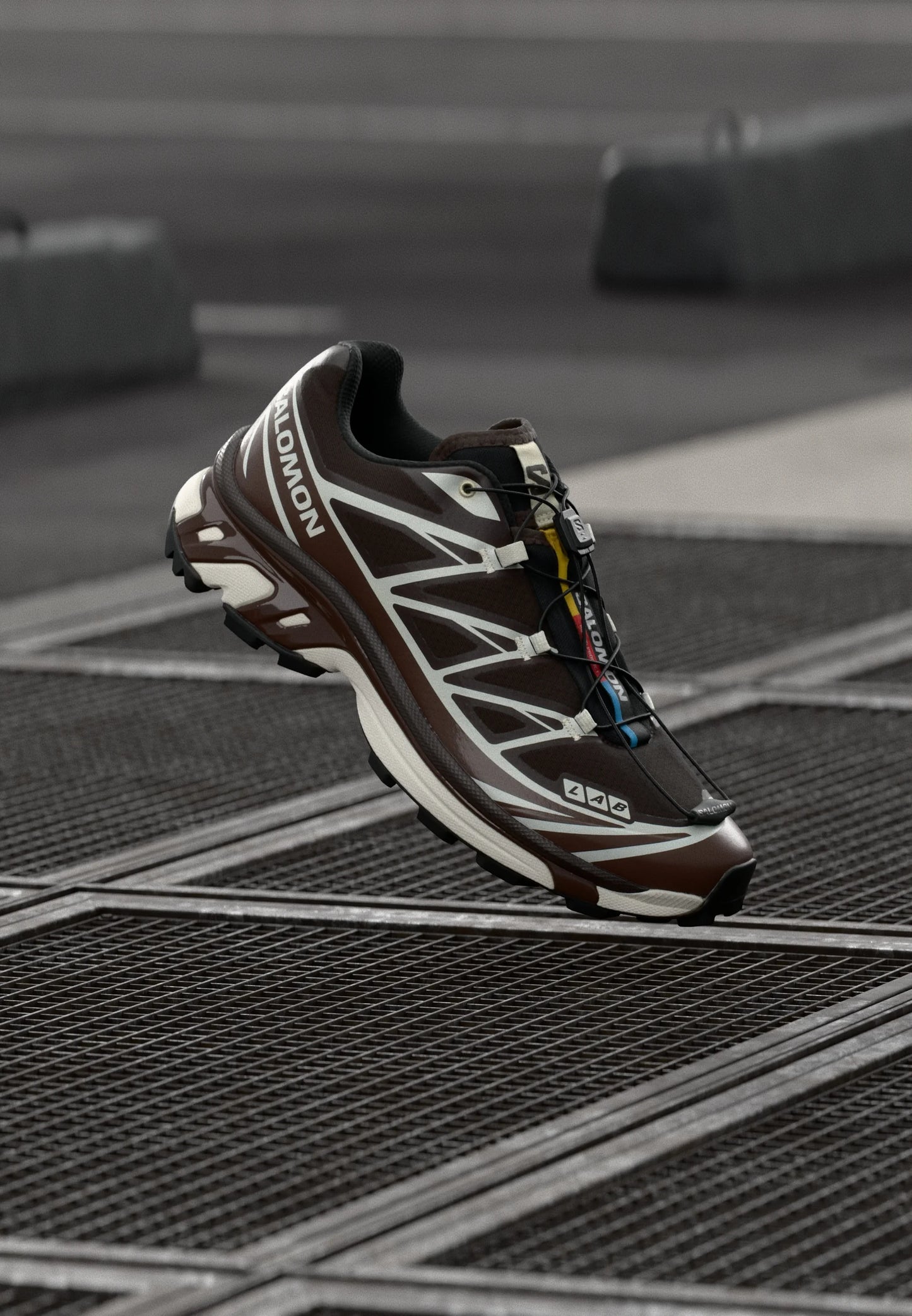 Scarpa da corsa marrone con accenti bianchi e tomaia in mesh. Presenta una suola testurizzata, un sistema di allacciatura rapida e un marchio visibile sul lato.