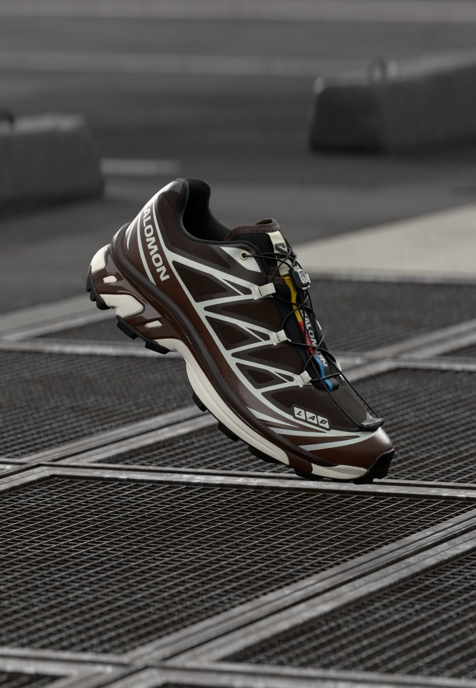 Scarpa da corsa marrone con accenti bianchi e tomaia in mesh. Presenta una suola testurizzata, un sistema di allacciatura rapida e un marchio visibile sul lato.