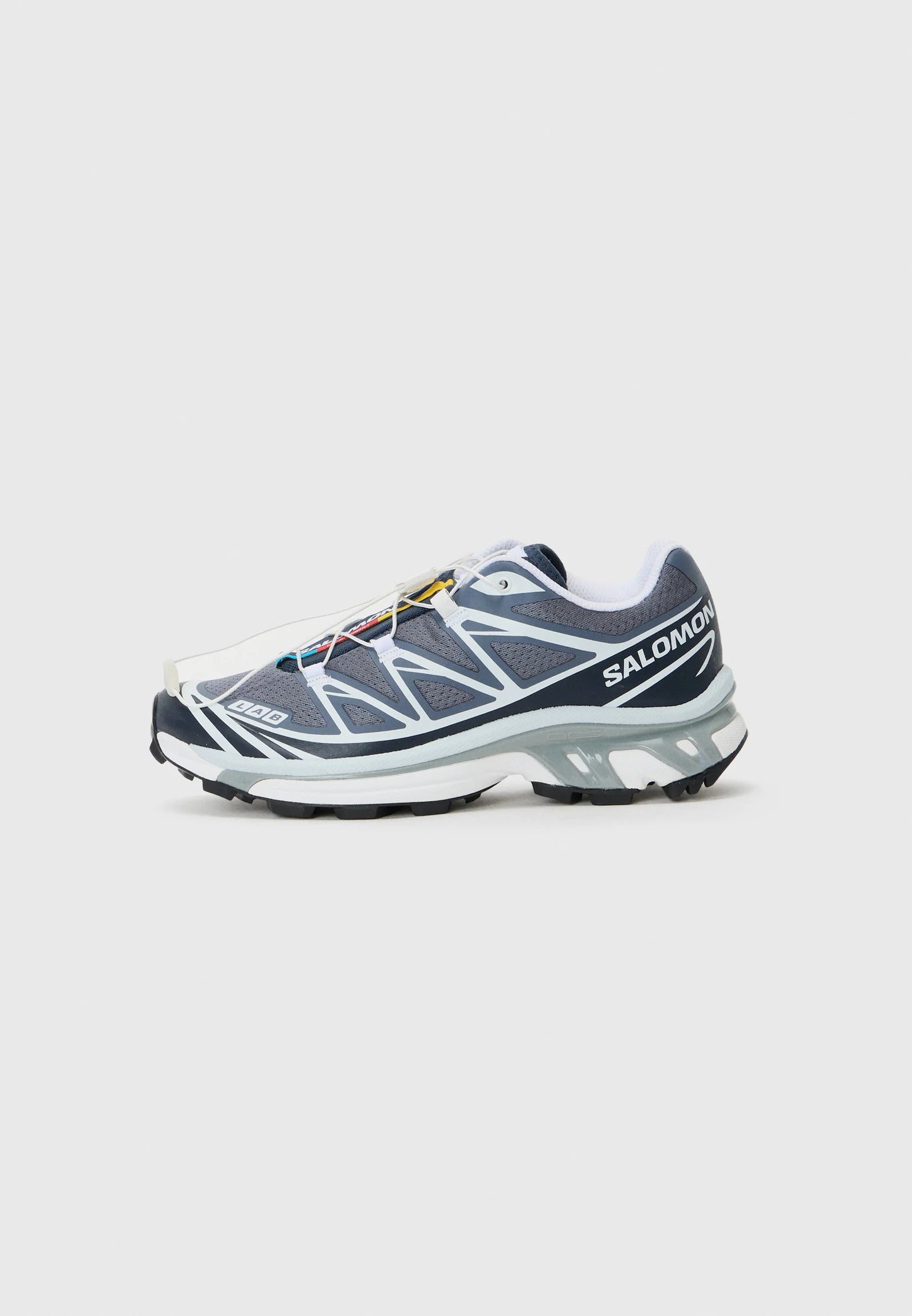 Scarpe sportive da uomo con tomaia in mesh grigio, accenti bianchi, suola in gomma nera e sistema di allacciatura rapida. Presentano dettagli testurizzati e logo.