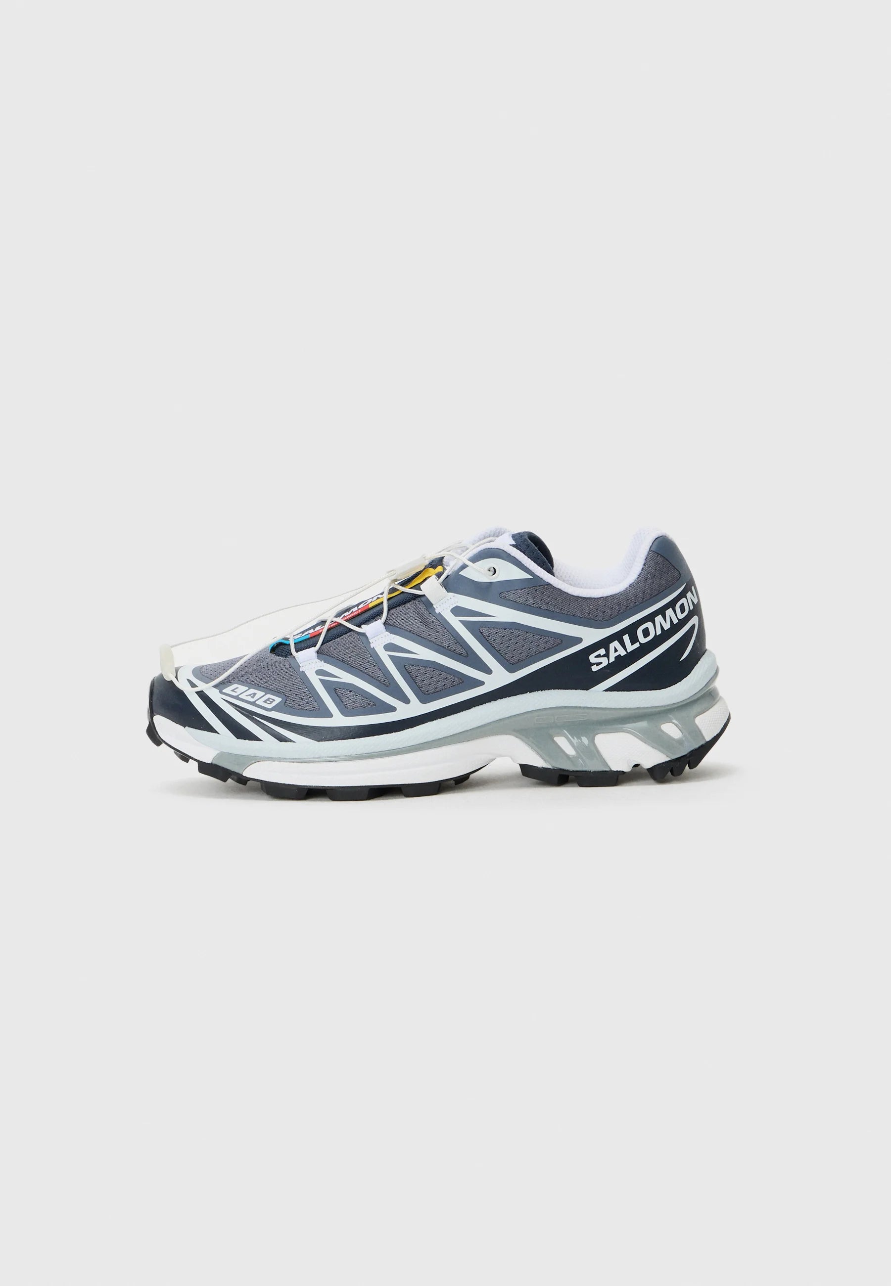 Scarpe sportive da uomo con tomaia in mesh grigio, accenti bianchi, suola in gomma nera e sistema di allacciatura rapida. Presentano dettagli testurizzati e logo.