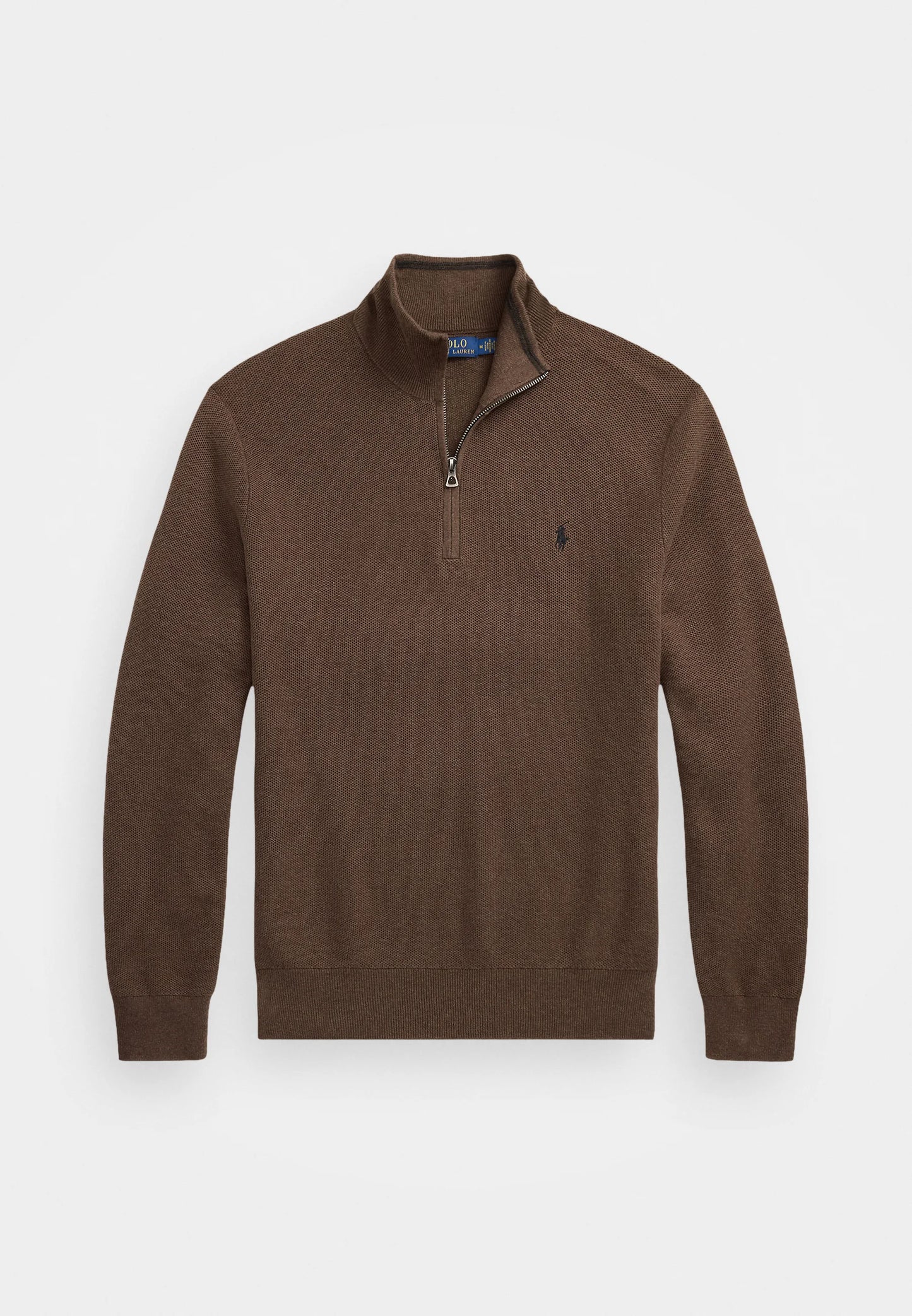 Suéter de punto marrón con cuello alto y cierre de cremallera. Debajo, se puede ver una camisa de rayas en azul claro. El modelo lleva pantalones oscuros y un cinturón.