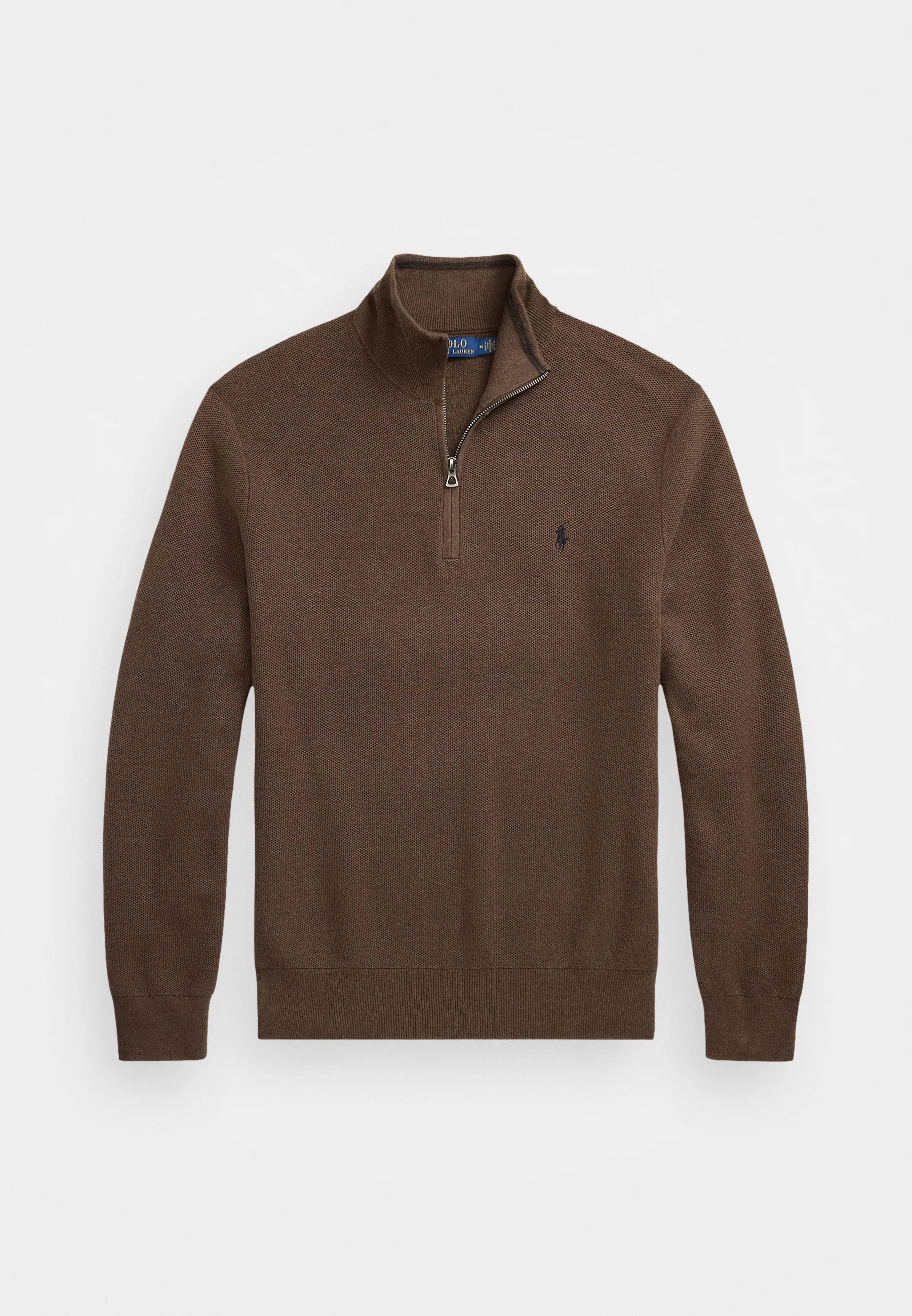 Suéter de punto marrón con cuello alto y cierre de cremallera. Debajo, se puede ver una camisa de rayas en azul claro. El modelo lleva pantalones oscuros y un cinturón.