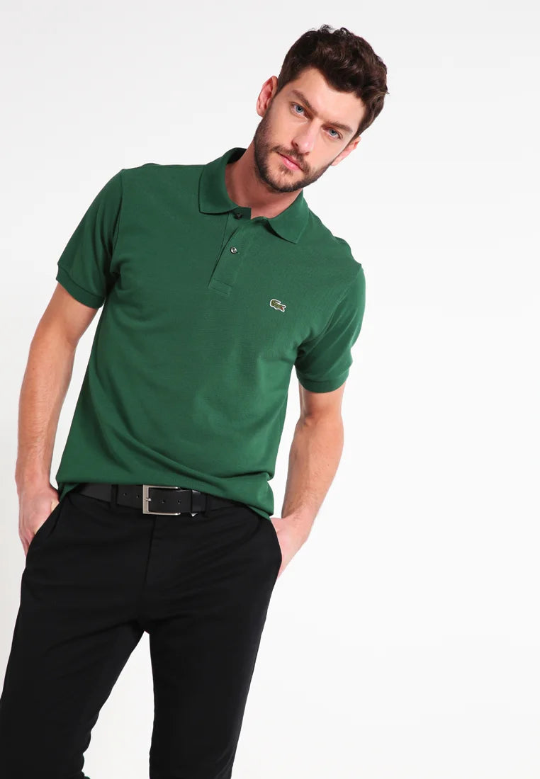 Polo shirt in cotone verde con colletto classico, maniche corte e un piccolo logo ricamato sul lato sinistro del petto. Abbinato a pantaloni neri.