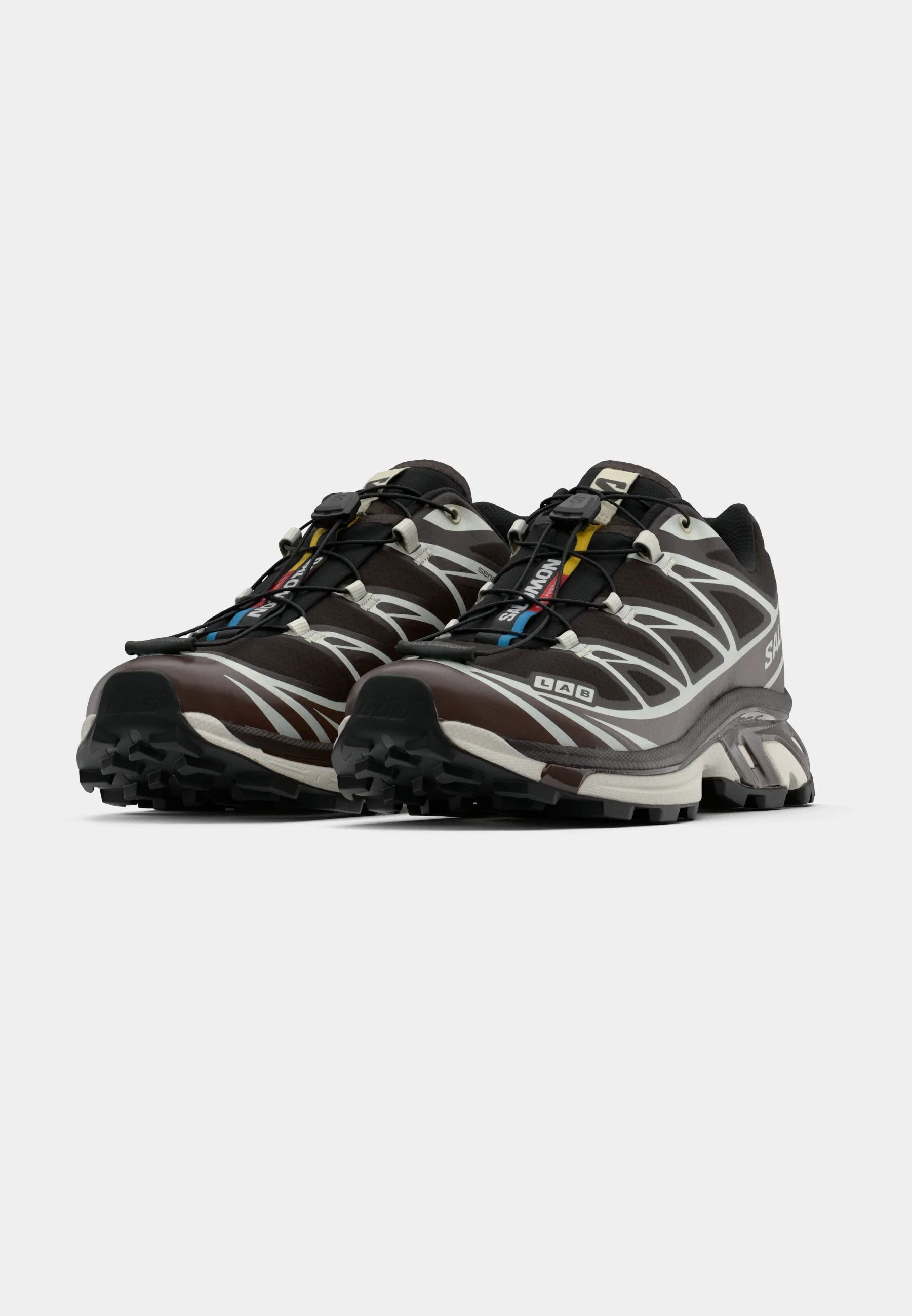 Scarpe da ginnastica marroni e grigie con suola nera, parte superiore testurizzata e dettagli riflettenti. Presentano un sistema di allacciatura rapida e un design con imbottitura.