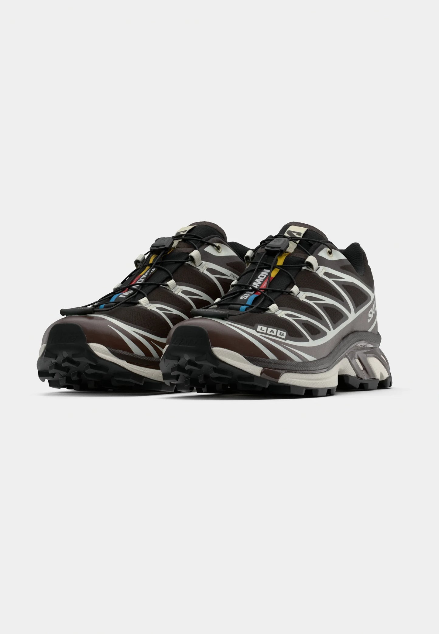 Scarpe da ginnastica marroni e grigie con suola nera, parte superiore testurizzata e dettagli riflettenti. Presentano un sistema di allacciatura rapida e un design con imbottitura.