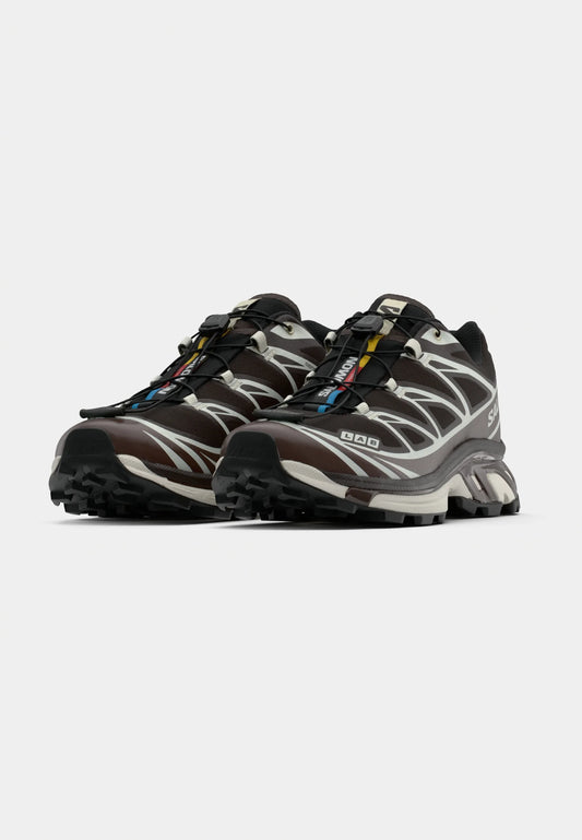 Scarpe da ginnastica marroni e grigie con suola nera, parte superiore testurizzata e dettagli riflettenti. Presentano un sistema di allacciatura rapida e un design con imbottitura.