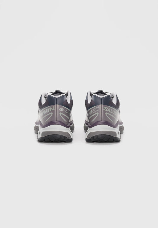 Scarpe da trail running nere e viola con accenti grigi, dotate di una suola testurizzata e di un sistema di laccio sicuro. Branding sulla parte laterale.
