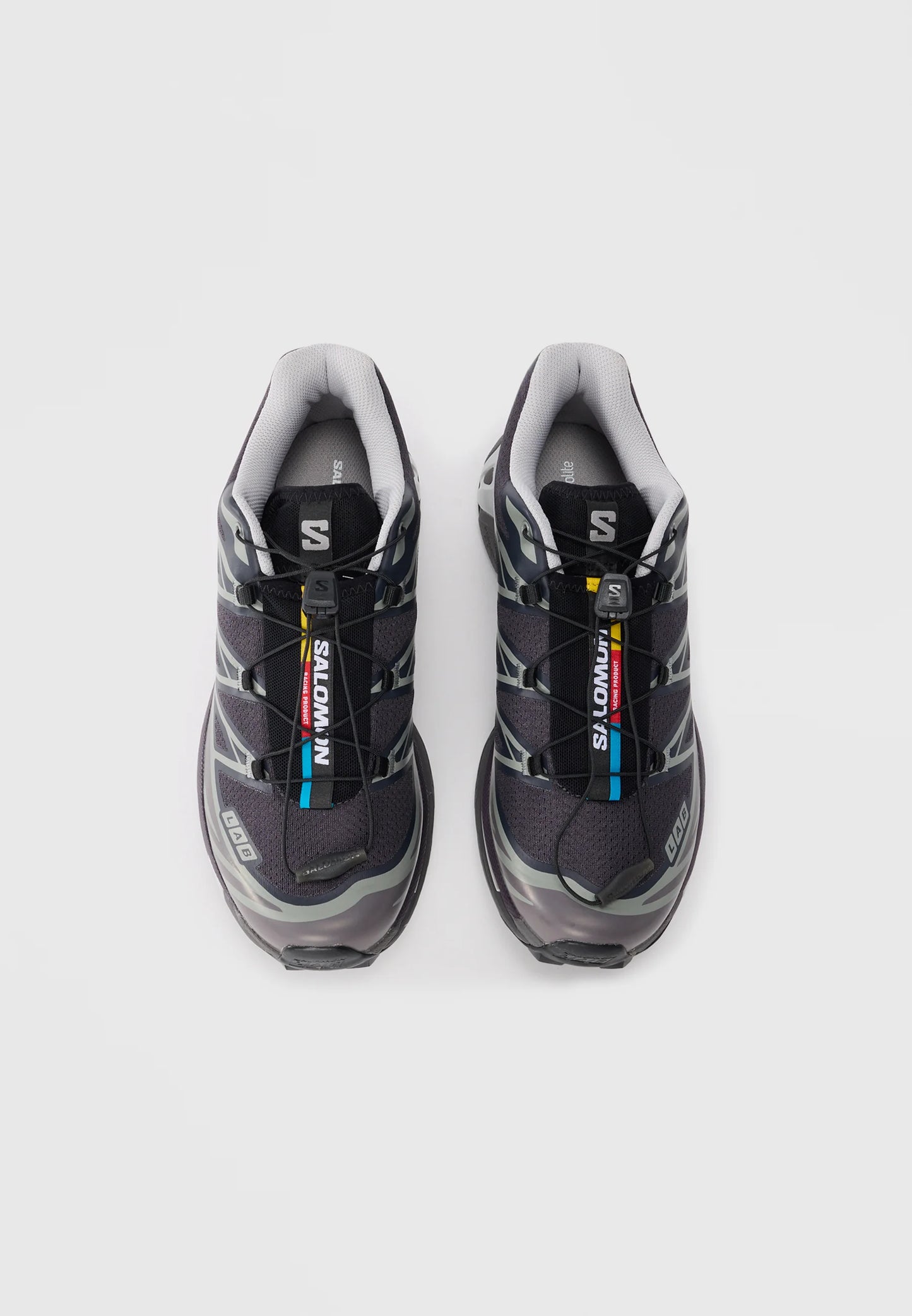 Scarpe da ginnastica nere con accenti grigi, tomaia in rete e sistema di allacciatura rapida. Presentano un interno imbottito e una suola in gomma testurizzata. Logo del marchio visibile.