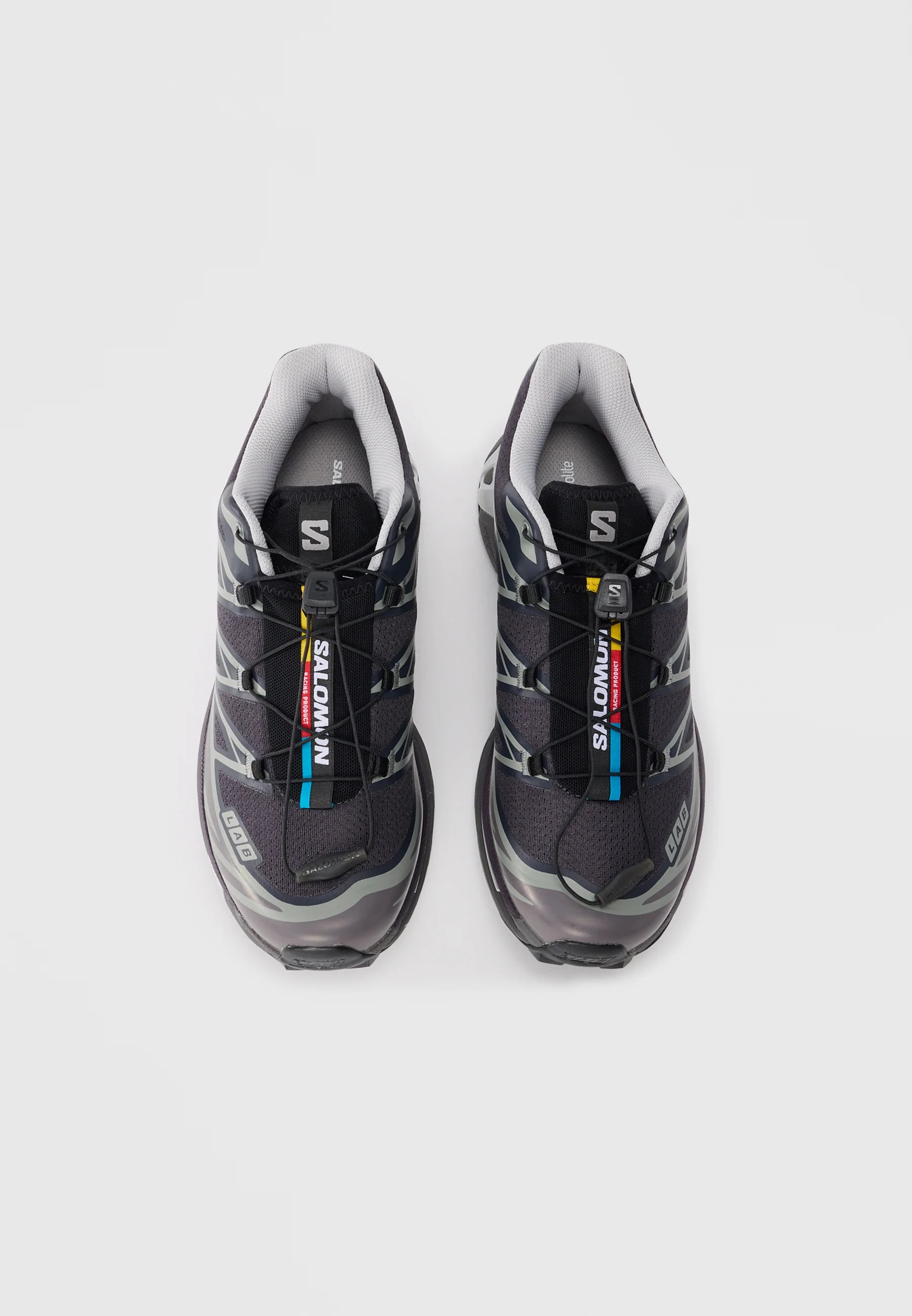 Scarpe da ginnastica nere con accenti grigi, tomaia in rete e sistema di allacciatura rapida. Presentano un interno imbottito e una suola in gomma testurizzata. Logo del marchio visibile.