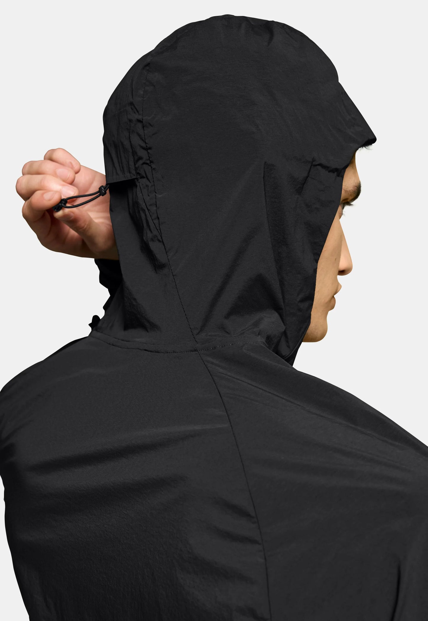 Giacca leggera nera con cappuccio aderente. Il materiale appare liscio e strutturato, con un cordino per regolare il cappuccio.