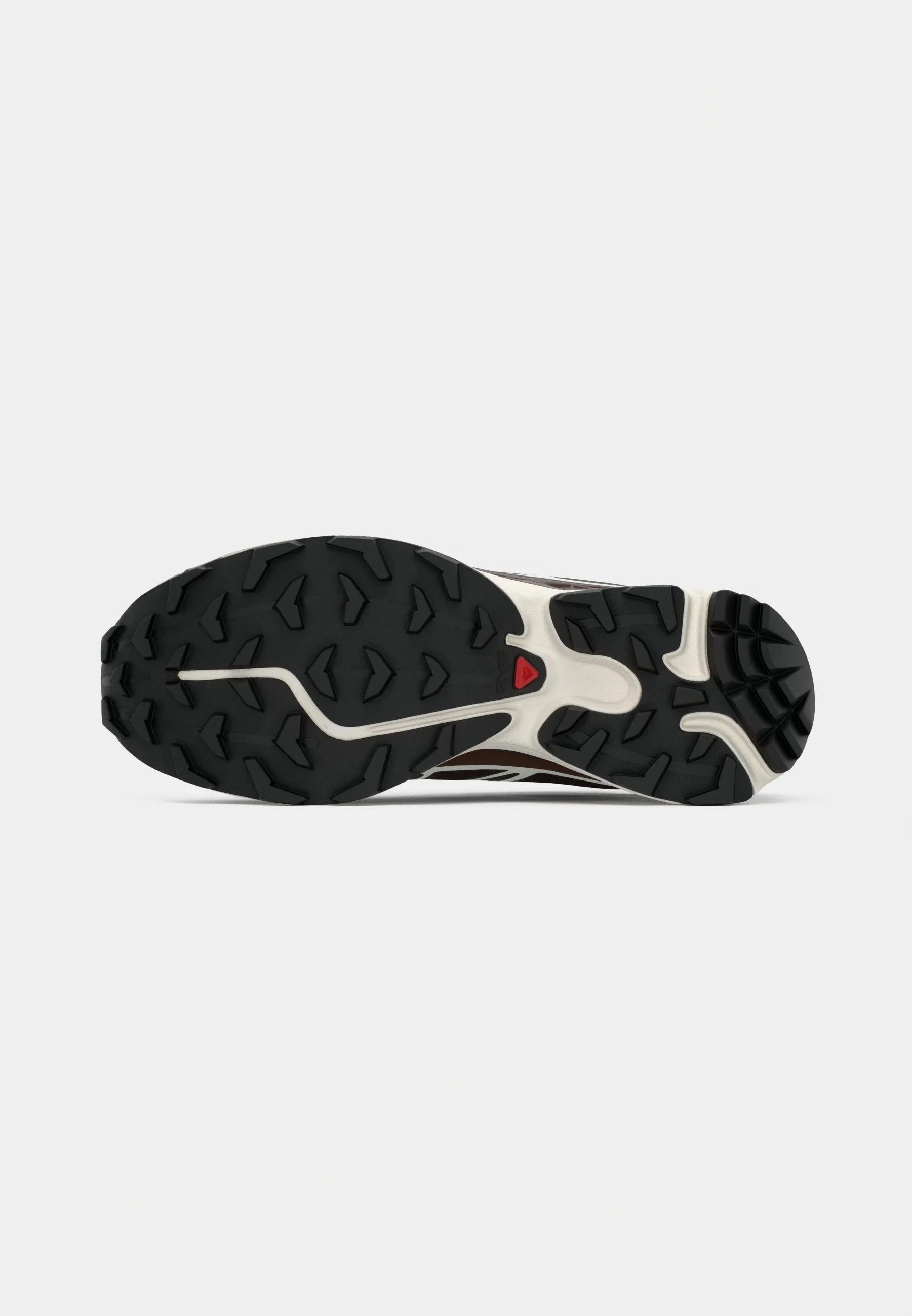 Suola di una scarpa da trail running, con un battistrada in gomma nera dotato di un motivo di grip dettagliato, un intersuola bianca e un accento rosso vicino all'arco.