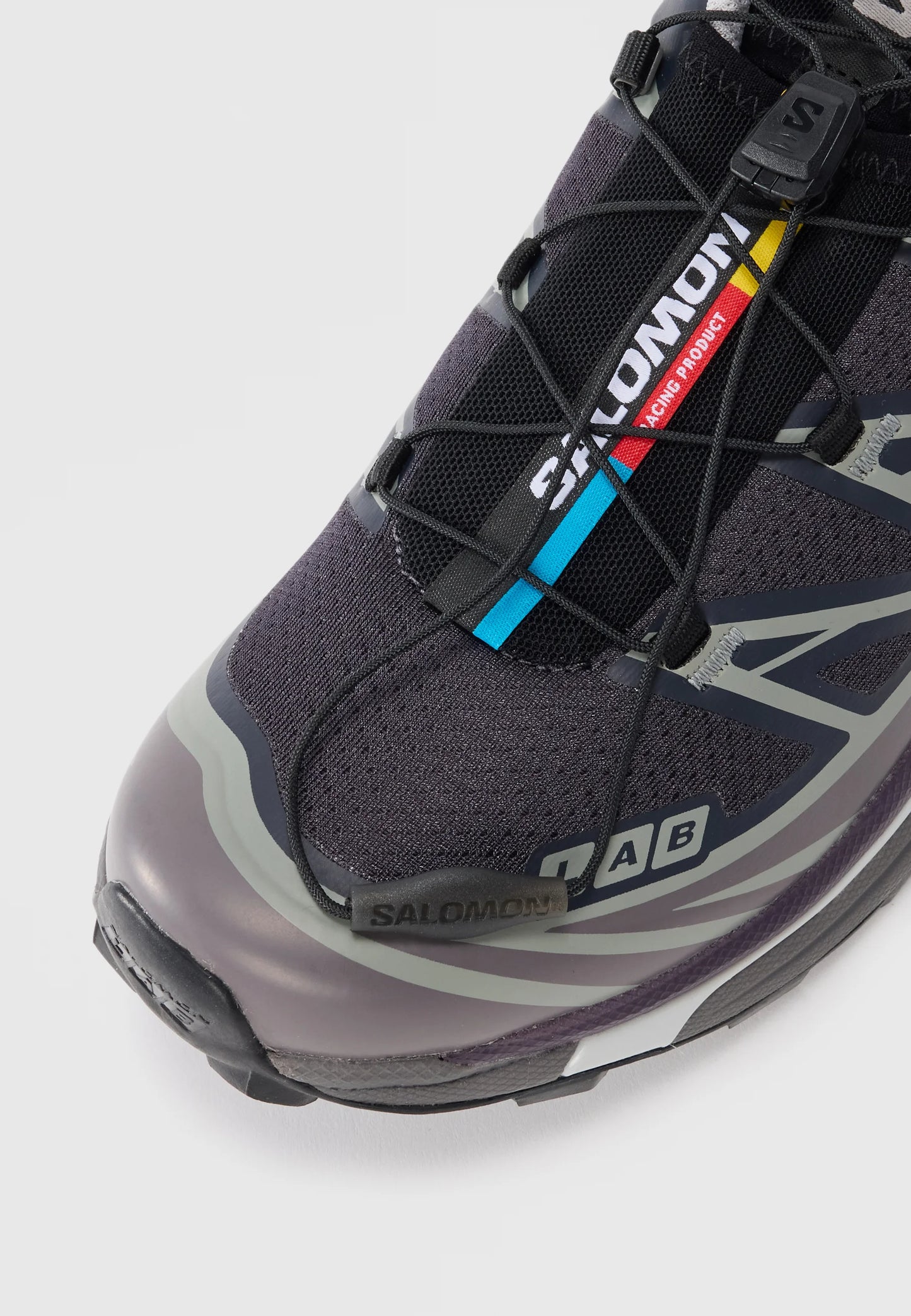 Scarpa sportiva nera e grigia con tomaia in rilievo, lacci sottili, punta in gomma e dettagli del logo in blu e rosso. Design leggero.