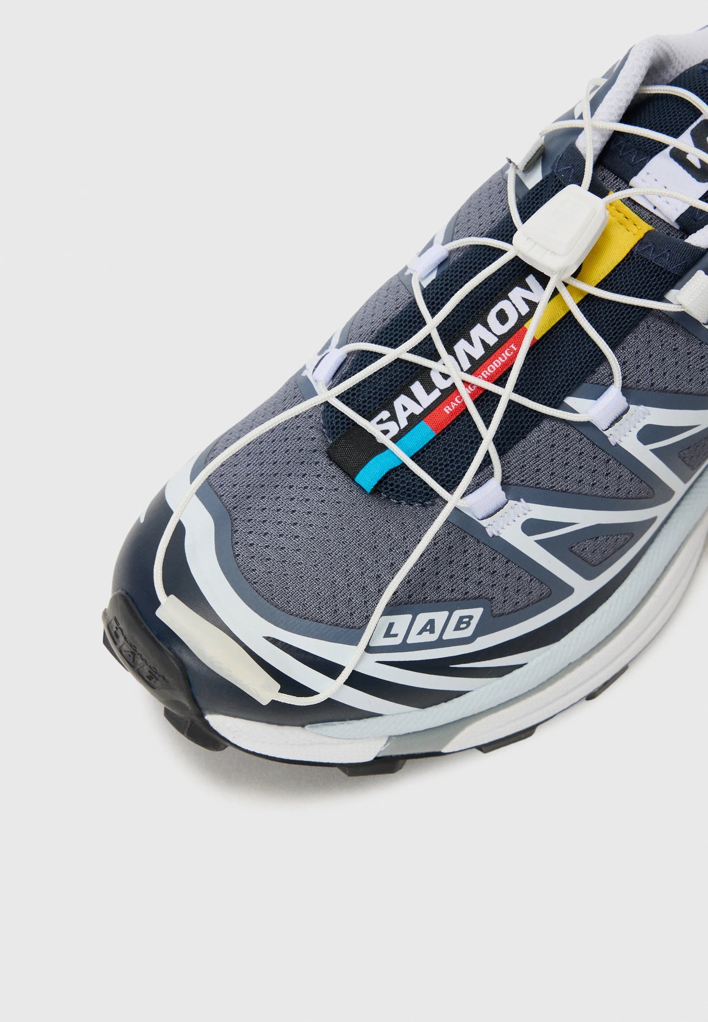 Scarpa sportiva grigia con tomaia in rete, suola in gomma e accenti bianchi. Presenta lacci elastici, una linguetta con marchio e una punta rinforzata.