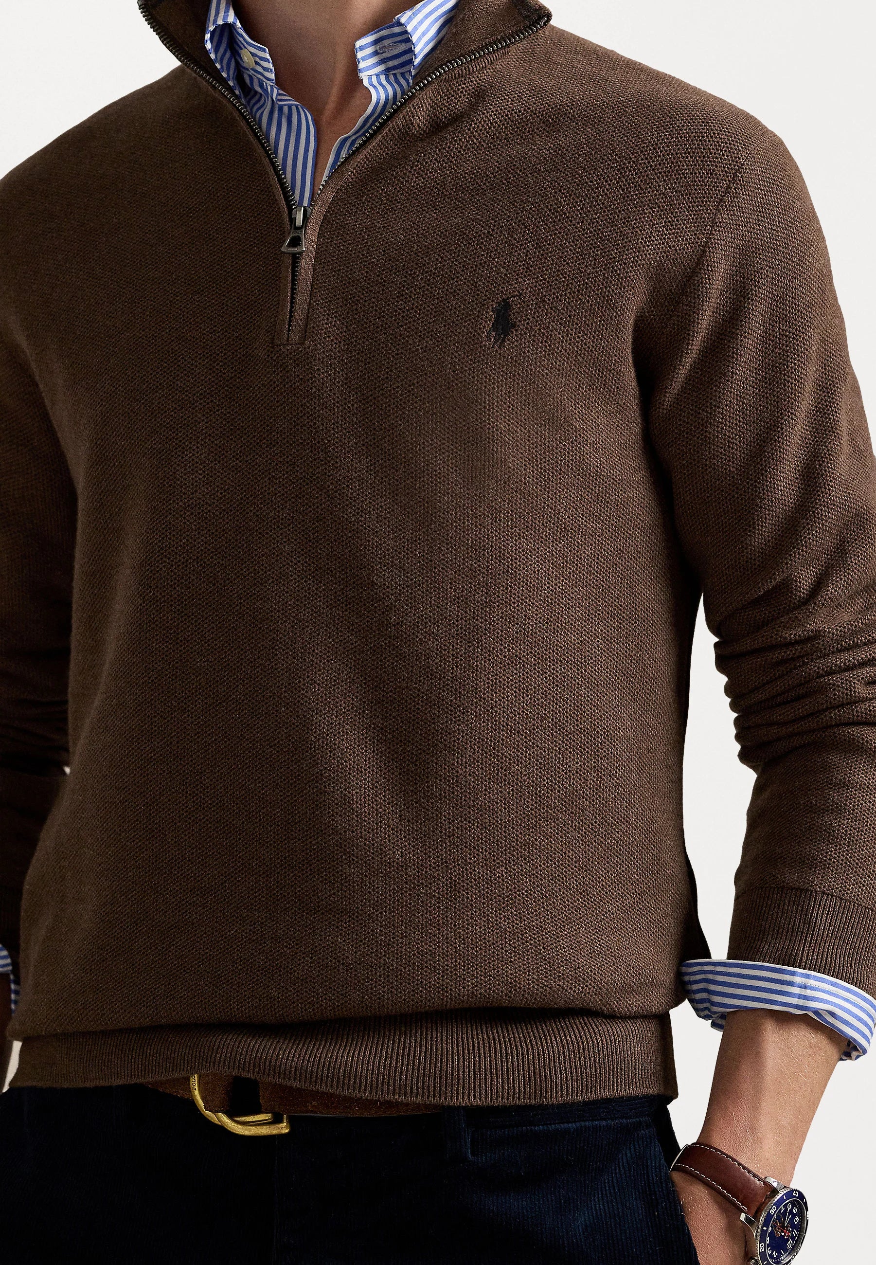 Suéter marrón con cuello de cremallera y tejido texturizado, que presenta un pequeño logo en el pecho, superpuesto a una camisa de rayas azul y blanca.