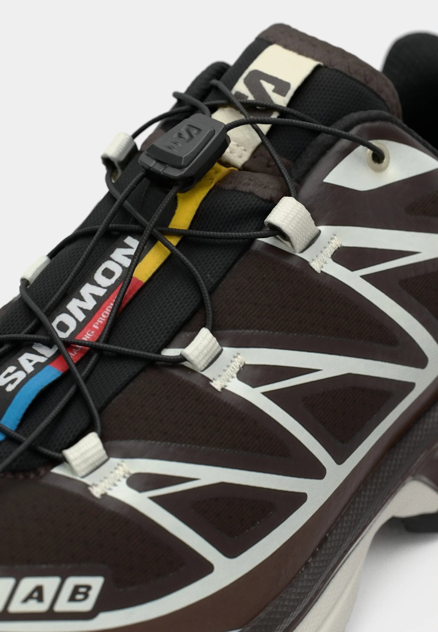 Scarpa da trail running marrone con tomaia in rete nera, dettagli riflettenti argentati e un sistema di allacciatura rapida con branding colorato.