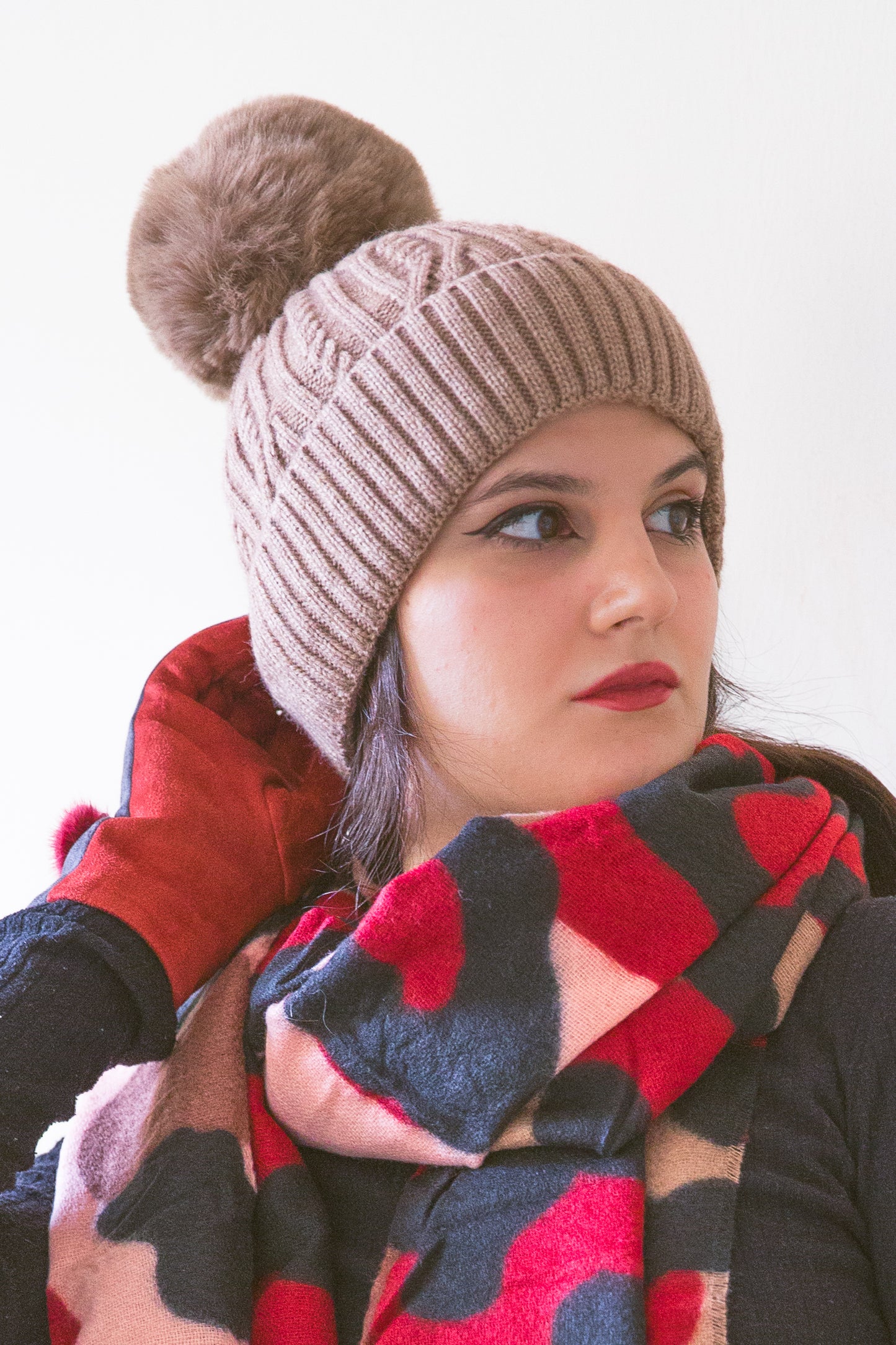 Donna con cappello invernale a trecce beige con pompon in pelliccia ecologica, abbinato a sciarpa colorata.